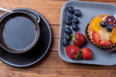 ahşap bir tabak ve masada kahve fincan üzerinde meyve tartlets,