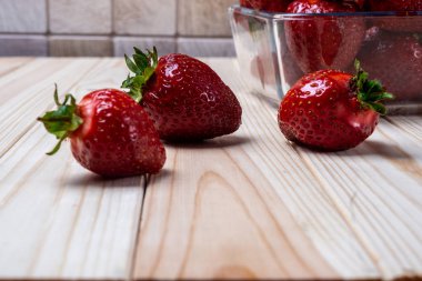 hafif ahşap bir masada ve kare cam bir kapta çilek
