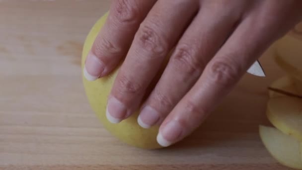 La mujer corta por el cuchillo la manzana a los trozos en la tabla de cortar a la mesa en la cocina — Vídeo de stock