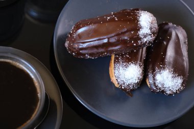 bir tabak ve bir fincan kahve üzerinde üç çikolata eclairs. gelenek