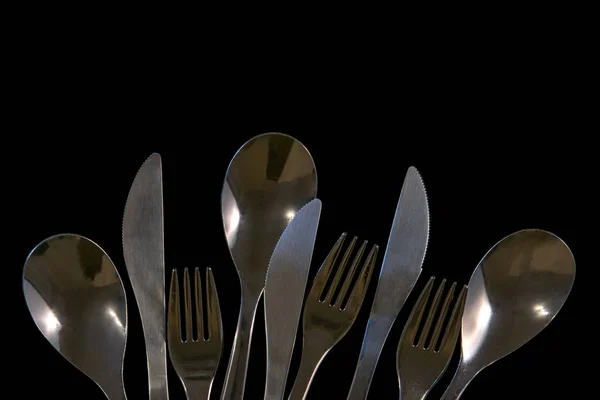 metal forks, knives and spoons on a black background. top view o