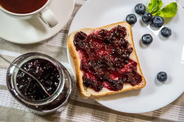 De toast met bosbessen jam en een kan met Huckleberry jam op een — Stockfoto