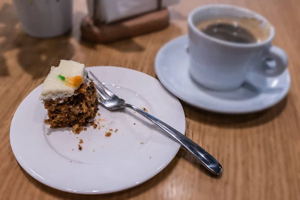 A piece of carrot cake on a white plate and cup of black coffee