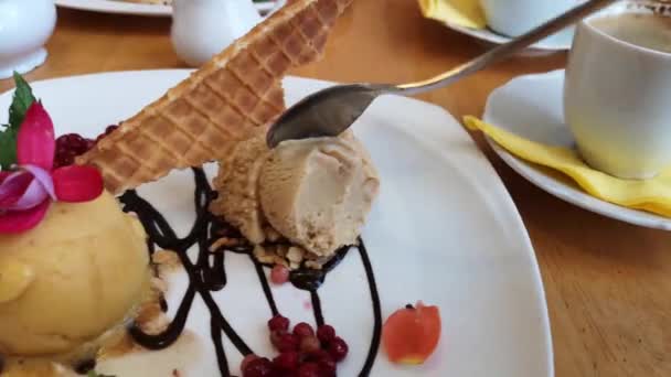 한 남자가 카페에서 와플과 신선한 베리로 장식된 석탄과 치커리 아이스크림을 먹습니다. 나무 테이블에서 아침 식사. — 비디오