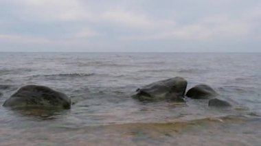 Bir taş plajda bulutlu bir günde Baltık Denizi dalgalarının hareketi. Arka planda