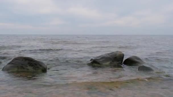 De beweging van de golven van de Oostzee op een bewolkte dag op een stenen strand. Op de achtergrond — Stockvideo