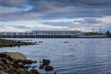 Taştan kıyıları olan geniş nehir üzerindeki hidroelektrik santrali.