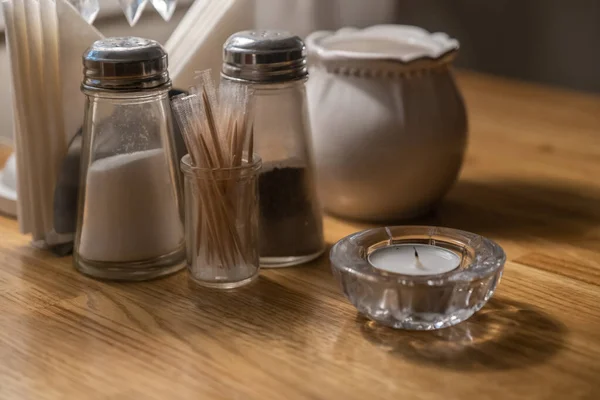 Salt shaker, pepper shaker, toothpicks and a candle on a table i