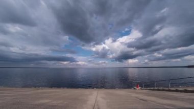 Beton bir gezinti güvertesi ve körfez zaman dilimi üzerinde alçak hareket eden yağmur bulutları. Sudaki bulutların yansıması..