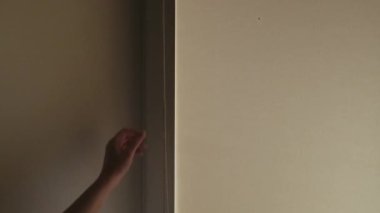 El, bayıltıcı tekerlekli jaluziyi açar. İçerideki pencerenin perdeleri var. Penceredeki bulutlar.