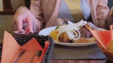 Bir kadın bir restoranda et yemeği yer. Taze sebzeli ve kızarmış patatesli kuzu kebabı.