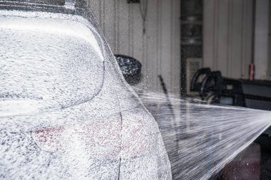 Araba yıkama işlemi, tamamen beyaz köpükle kaplı ve su tabancasından sıçramış..