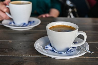 Kafedeki bir masada bir fincan sıcak kahve. Elinde bir fincan beyaz latte tutan kadın..
