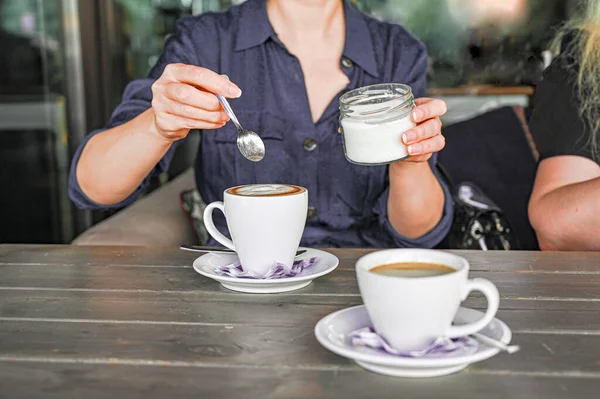 woman pours sugar into hot black coffee in a cafe in the morning.