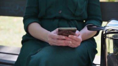 Bir kadın park bankında otururken cep telefonunda kurye kullanıyor..