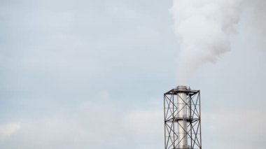 Mavi gökyüzüne karşı beyaz dumanların çıktığı fabrika metal borusu..