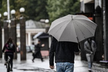 Bir adam gri bir şemsiyenin altında caddede yürür. Sonbahar başlarında yağmur yağar.