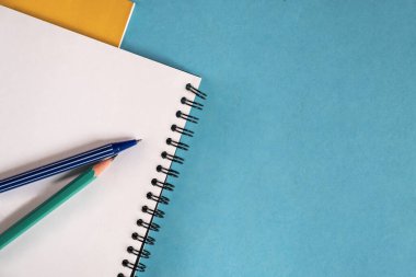 Beyaz sayfalı boş spiral not defteri ve mavi bir masada birkaç kalem..