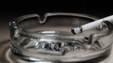 Tipik bir cam kül tablasının kenarında yanan bir sigara. Sigarayı bırak..