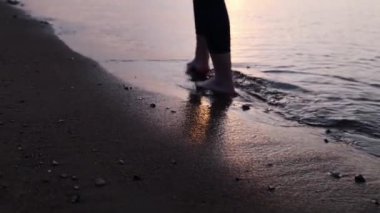 Siluet Bacaklar suyun üzerinde yürürken yakın plan. Sahilde gün batımına karşı yürüyen bir kadın..