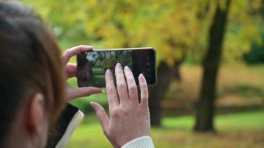 Bir kadın telefonuyla güzel bir sonbahar manzarasının fotoğrafını çekiyor..