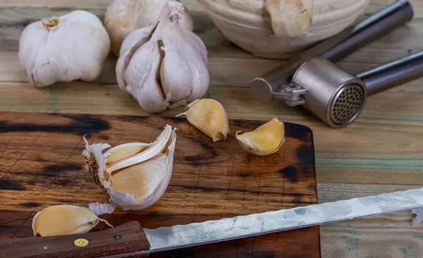 Garlic and garlic press in the kitchen on the board.