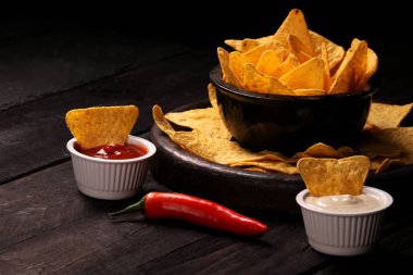 Ahşap kase tortilla cips siyah ahşap zemin üzerine biber biber sosu, salsa ve peynir dip ile Meksika cips