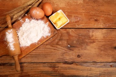 Mutfak haddeleme pin, ahşap arka planda un ile ahşap kase, masada kruvasan yapmak için yumurta ve tereyağı.