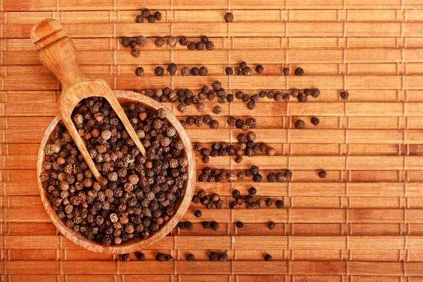 Hölzerne Servierlöffelschaufel voll schwarzer Pfeffer Gewürzkugeln in Holzschüssel isoliert über dem hölzernen Hintergrund — Stockfoto