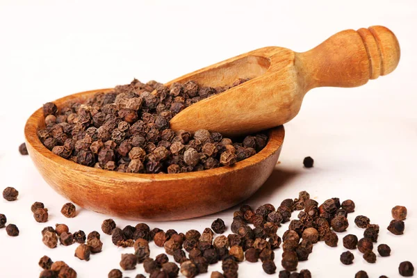 Wooden serving spoon shovel full of black pepper spice balls in wooden bowl isolated over the white background