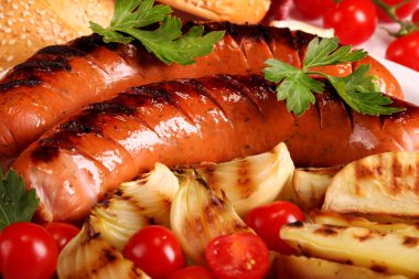 Beyaz ahşap masa üzerinde beyaz tabakta sebze, baharat ve ekmek ile ızgara sosis