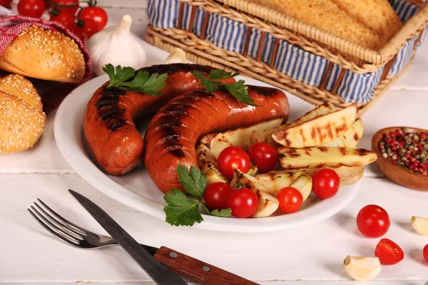 Grillwürste mit Gemüse, Gewürzen und Brot im weißen Teller auf weißem Holztisch — Stockfoto