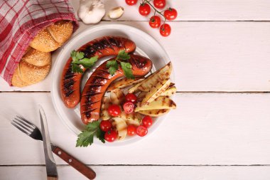 Beyaz ahşap masa üzerinde beyaz tabakta sebze, baharat ve ekmek ile ızgara sosis. Üstte görüntü.