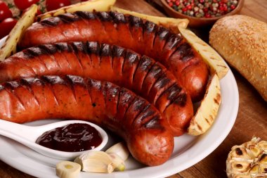 Ahşap masa üzerinde beyaz tabakta sebze, baharat ve ekmek ile ızgara sosis