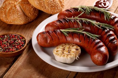 Ahşap masa üzerinde beyaz tabakta sebze, baharat ve ekmek ile ızgara sosis