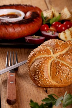 Ahşap masa üzerinde siyah tabakta sebze, baharat ve ekmek ile ızgara sosis. Makro görünümünü kapat.