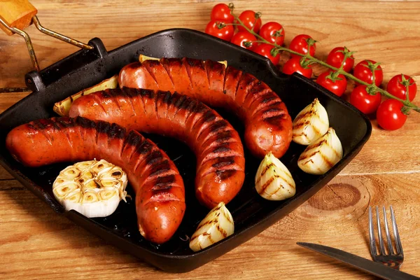 Grilled sausages with vegetables and spices in a pan on wooden background — Stock Photo, Image