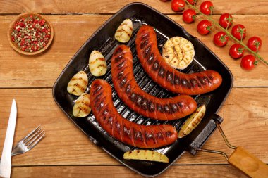 Ahşap arka plan üzerinde bir tavada sebze ve baharat ile ızgara sosis. Üstte görüntü