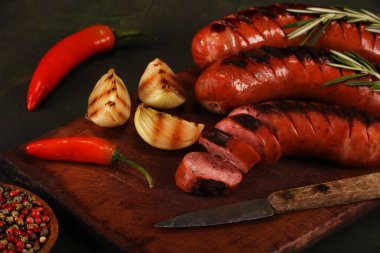 Ahşap kesme tahtası arka planda sebze, baharat ve ekmek ile ızgara sosis