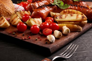 Ahşap kesme tahtası arka planda sebze, baharat ve ekmek ile ızgara sosis