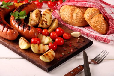 Ahşap kesme tahtası arka planda sebze, baharat ve ekmek ile ızgara sosis
