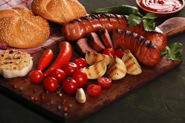 Grilled sausages with vegetables, spices and bread on wooden cutting board background — Stock Photo, Image