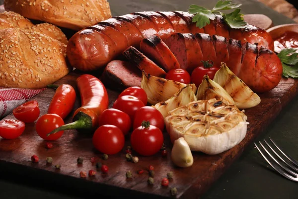 Grilled sausages with vegetables, spices and bread on wooden cutting board background — Stock Photo, Image