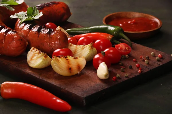 Salsichas grelhadas com legumes, especiarias e pão sobre fundo de tábua de corte de madeira — Fotografia de Stock