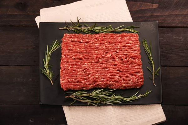 raw minced meat on paper, ingredients for burger with tomato, pepper, onion, spices and seasonings on black background. Top view and copy space