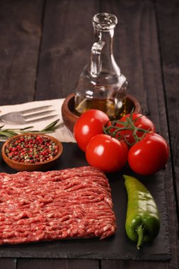 tabakta çiğ kıyma, siyah arka plan üzerinde domates, biber, soğan, baharat ve baharat ile burger için malzemeler.