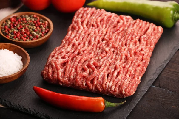 Carne picada crua no prato, ingredientes para hambúrguer com tomate, pimenta, cebola, especiarias e temperos em fundo preto . — Fotografia de Stock