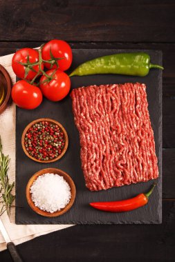 tabakta çiğ kıyma, siyah arka plan üzerinde domates, biber, soğan, baharat ve baharat ile burger için malzemeler.