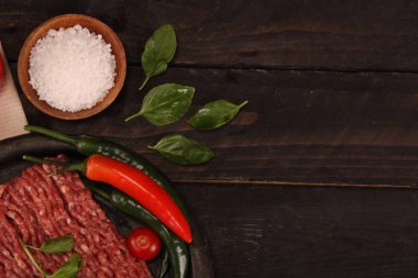 tabakta çiğ kıyma, siyah arka plan üzerinde domates, biber, soğan, baharat ve baharat ile burger için malzemeler.