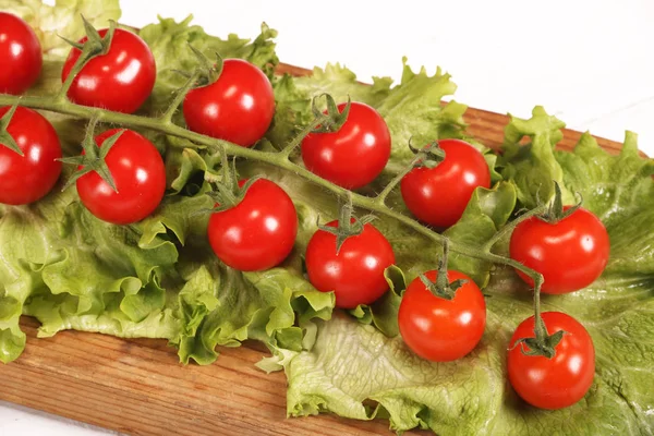 Brunch orgânico suculento fresco maduro de tomates cereja na tábua de corte com alface verde em uma mesa branca — Fotografia de Stock